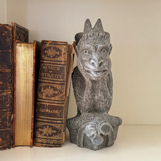 This Gargoyle figurine has his hands on his face and is deep in thought.  The figurine is holding up three books on white shelf against a white wall. House Parts home decor handmade Atlanta gargoyle grotesque whimsical fantasy mystical creature. Unique gift for fans of fantasy, dungeon, or dinosaurs. Unique Christmas gift for someone who has everything or fantasy lovers. Gothic, medieval, unique, artisan, craft, detail, specialty, a gift that no one else has, special