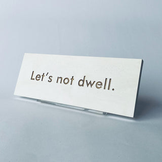 A rectangular white plaque with the phrase 'Let's not dwell' on a colored background. Stand sold separately

House Parts handmade, crafted, artisan, high quality, statues, busts, and garden and animal figurines.  Unique gifts for everyone. Indoor decorations, Outdoor statues and garden items. Fantasy, whimsical, thoughtful gifts, original gift idea, shop small business, plaster, concrete, Clam shell, Gargoyles, Alice in Wonderland, animal lover gifts, pet memorial