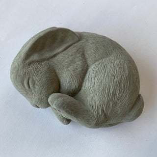 Plaster sculpture of a sleeping bunny made from gray concrete, with a textured finish on a white background.  Peacefully dreaming bunny.  Sweet dreams little bunny

House Parts handmade, crafted, artisan, high quality, statues, busts, and figurines.  Unique gifts for everyone. Indoor decorations, Outdoor statues and garden items. Thoughtful gift, animal lovers, rabbit lovers, instead of pet, small business, female owned family business, rabbit, bunny, dog, turtle, frog, clam shell